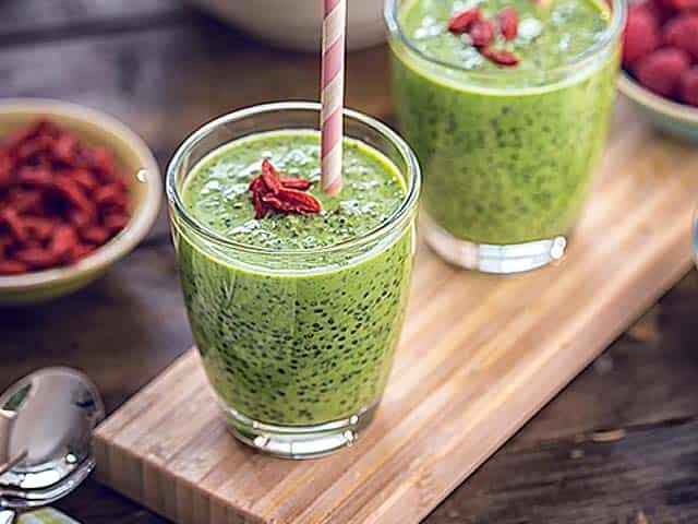 Green smoothies with goji berries on top and a bowl of raspberries