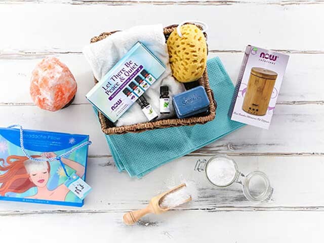 essential oils in basket with spa accessories and bag on white wood