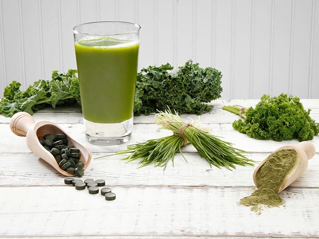 Smoothie with a variety of Green Superfoods and vitamin supplements on white wood table