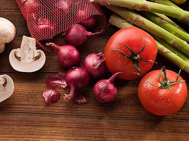 Mushrooms, asparagus, tomatoes and bag of shallots on brown wood