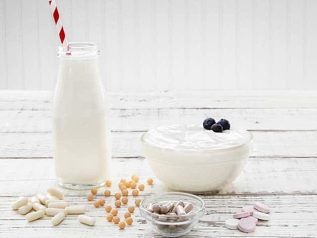 Vitamins, bottle of milk and bowl of yogurt with blueberries on white wood