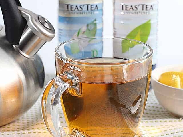 Tea in a mug and kettle with bowl of lemon and two bottles of tea in background