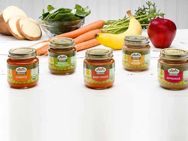 Different Sprouts baby food jars with fresh vegetables in background