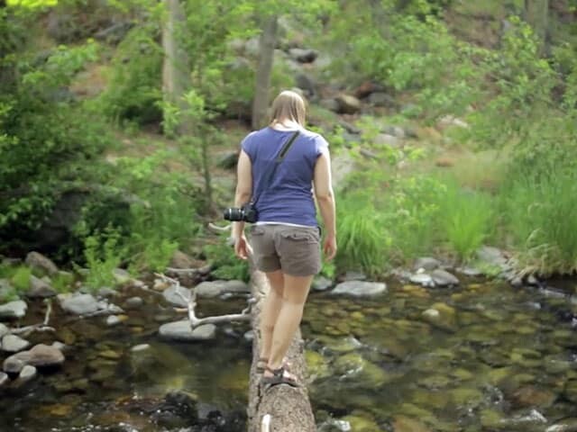 woman crossing river on log