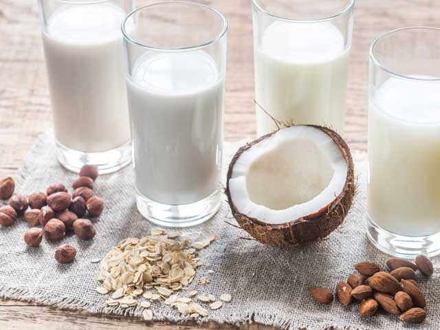 Four glasses of Alternative Milk and Vegan Substitutes with half a coconut, raw almonds and oats