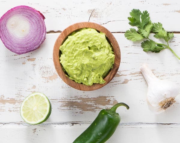 Classic guacamole in a bowl surrounded by ingredients