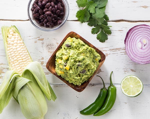 Southwest guacamole in a bowl surrounded by ingredients