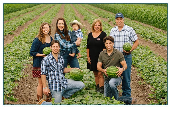 Little Bear Produce family of farms standing in a field holding melons.